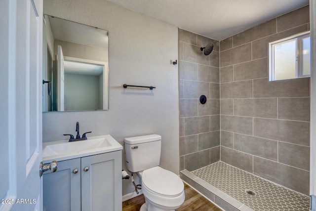 full bath with tiled shower, toilet, wood finished floors, a textured ceiling, and vanity