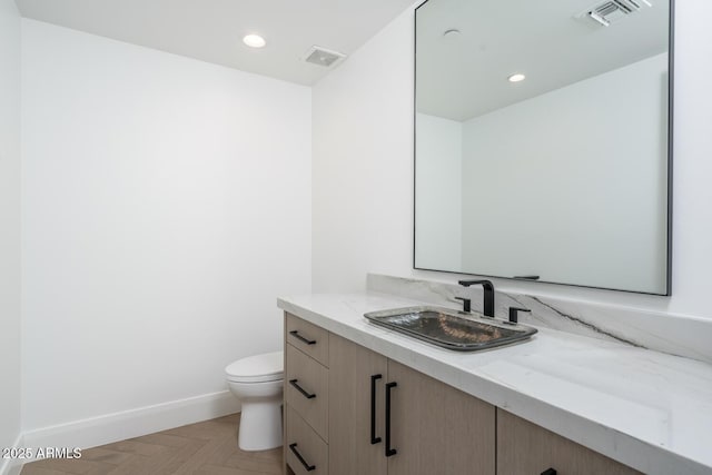 bathroom with parquet flooring, vanity, and toilet