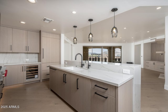 kitchen with sink, beverage cooler, light stone counters, decorative light fixtures, and light brown cabinetry