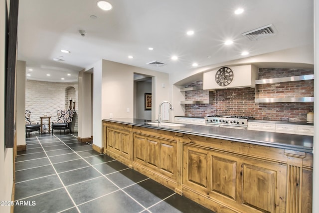 kitchen with brick wall, stainless steel counters, sink, dark tile patterned flooring, and stovetop