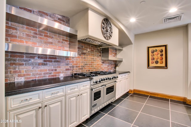 kitchen with white cabinetry, double oven range, dark tile patterned floors, and wall chimney range hood