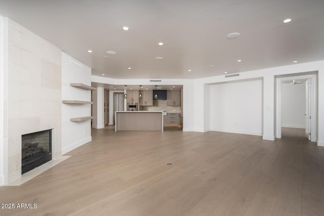 unfurnished living room featuring a tiled fireplace and light wood-type flooring