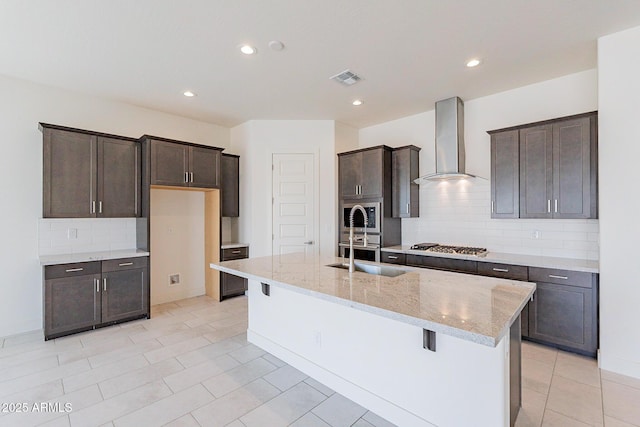 18950 W Ocotillo Rd, Waddell, AZ 85355 - kitchen featuring wall chimney exhaust hood, a center island with sink, tasteful backsplash, visible vents, and light stone countertops