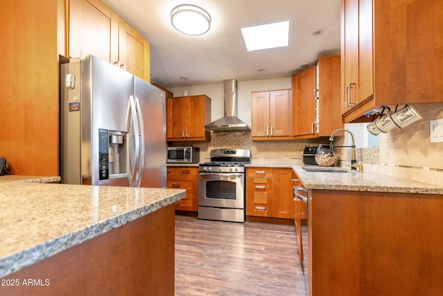 kitchen featuring a sink, wall chimney range hood, backsplash, and stainless steel appliances