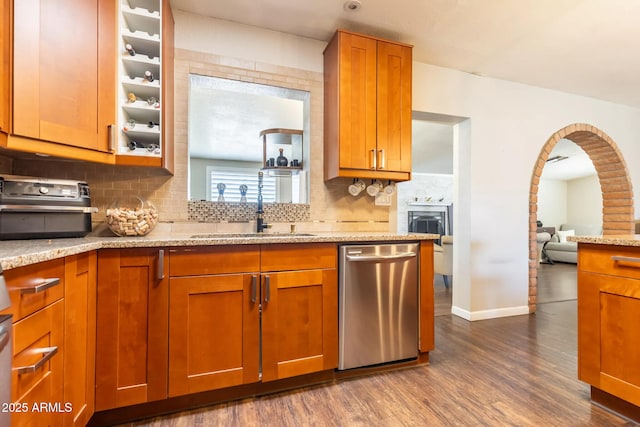 kitchen featuring stainless steel dishwasher, brown cabinetry, light stone counters, dark wood-style flooring, and decorative backsplash