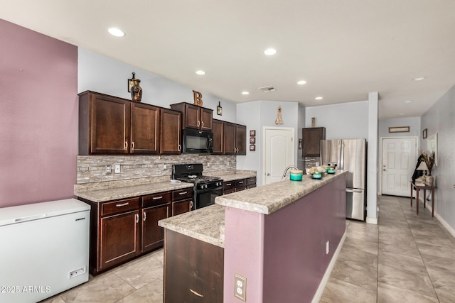 kitchen featuring tasteful backsplash, visible vents, a kitchen island with sink, dark brown cabinets, and black appliances