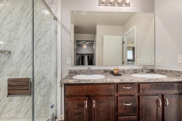 bathroom with double vanity, a walk in closet, a sink, and a marble finish shower