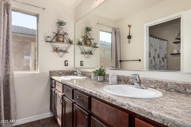 full bath featuring baseboards, wood finished floors, double vanity, and a sink