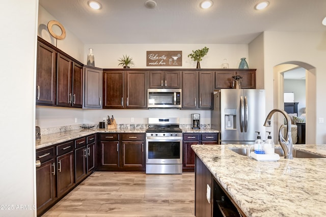 kitchen featuring light stone counters, stainless steel appliances, light hardwood / wood-style floors, and dark brown cabinetry