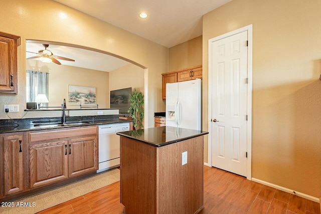 kitchen with white appliances, light wood-style flooring, arched walkways, and a sink