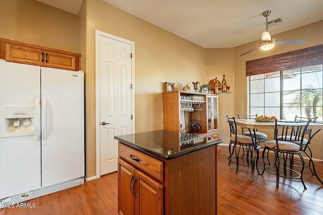 kitchen with white refrigerator with ice dispenser, visible vents, brown cabinetry, a kitchen island, and wood finished floors