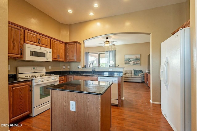 kitchen featuring white appliances, a kitchen island, wood finished floors, a peninsula, and a sink