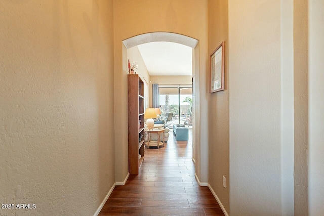 hallway with baseboards, arched walkways, dark wood finished floors, and a textured wall