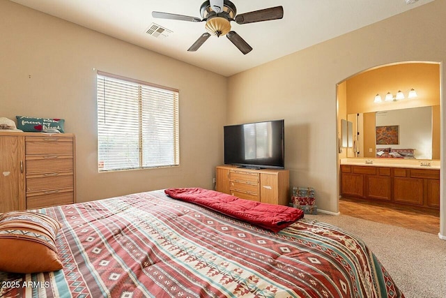 bedroom with light carpet, visible vents, arched walkways, a ceiling fan, and ensuite bath