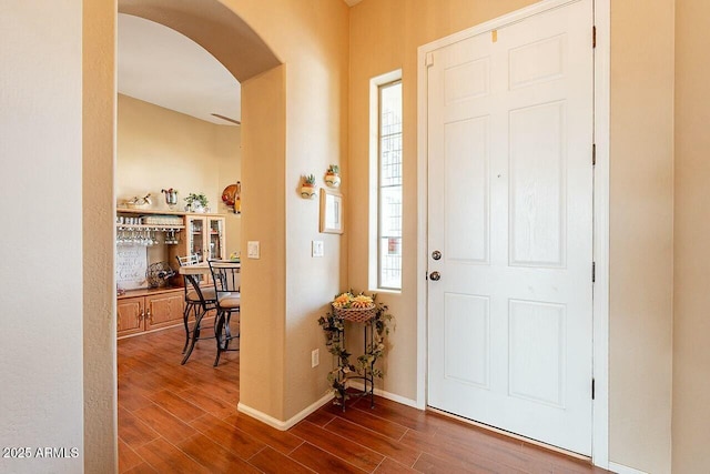 foyer featuring baseboards, arched walkways, and dark wood-type flooring