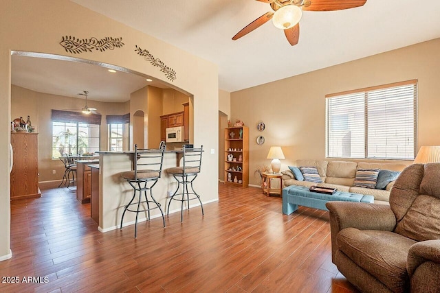 living room featuring arched walkways, ceiling fan, wood finished floors, and baseboards