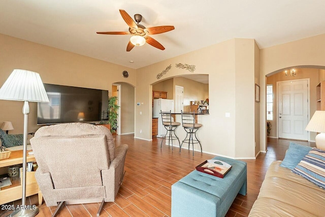 living room with arched walkways, ceiling fan, wood finished floors, and baseboards