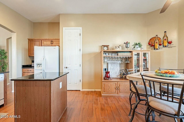 kitchen featuring white appliances, baseboards, light wood-type flooring, a center island, and dark countertops