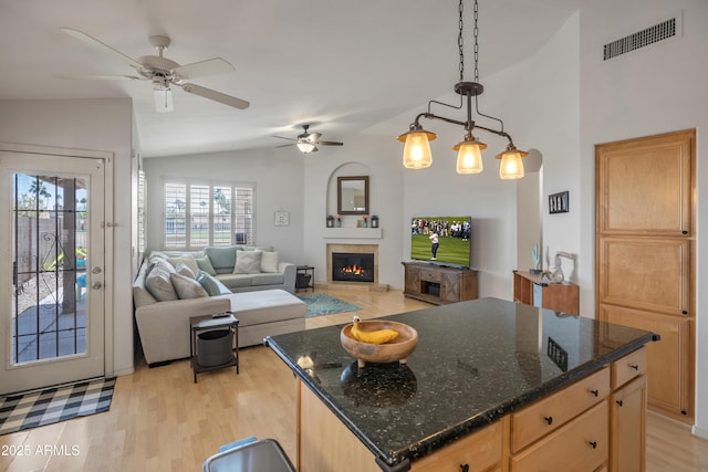 kitchen featuring pendant lighting, visible vents, light wood-style flooring, a glass covered fireplace, and vaulted ceiling