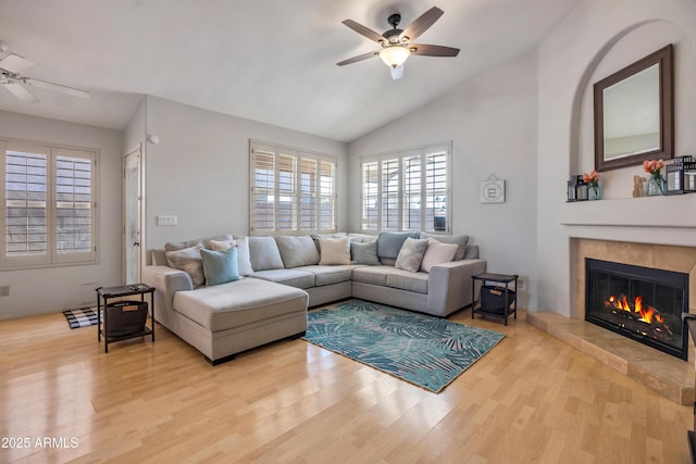 living room with lofted ceiling, light wood finished floors, a ceiling fan, and a tile fireplace