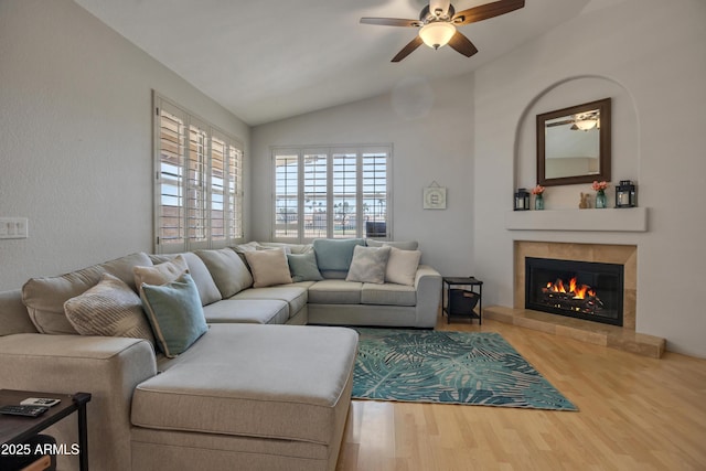 living room with ceiling fan, a tile fireplace, vaulted ceiling, and wood finished floors