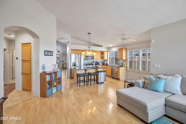 living room with light wood-style floors, arched walkways, ceiling fan, and lofted ceiling