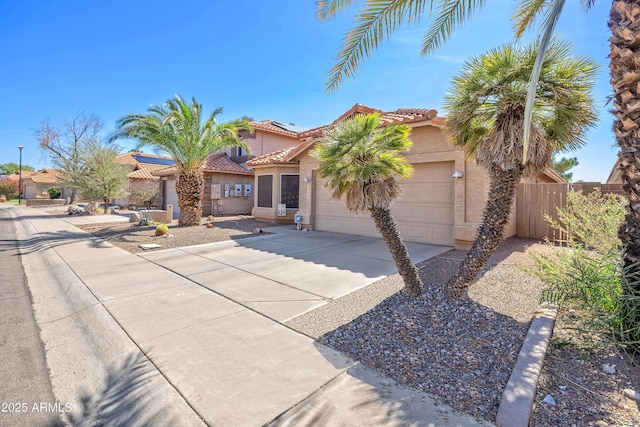 mediterranean / spanish house featuring driveway, a tile roof, an attached garage, fence, and stucco siding