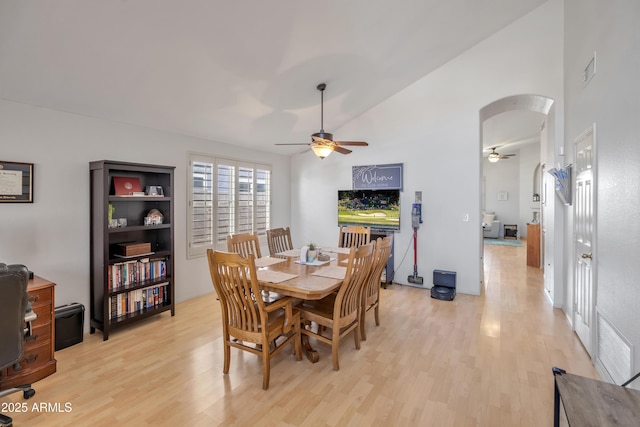 dining room with arched walkways, ceiling fan, light wood finished floors, and vaulted ceiling