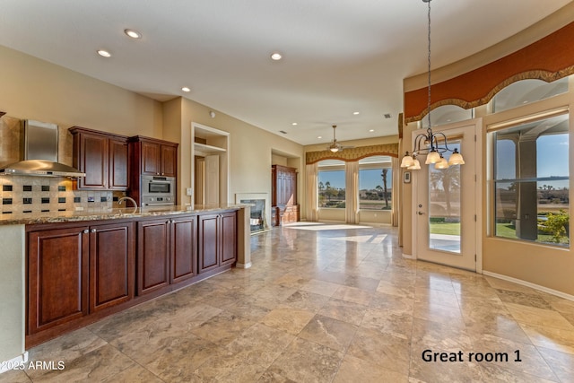 kitchen featuring tasteful backsplash, pendant lighting, sink, wall chimney exhaust hood, and light stone counters