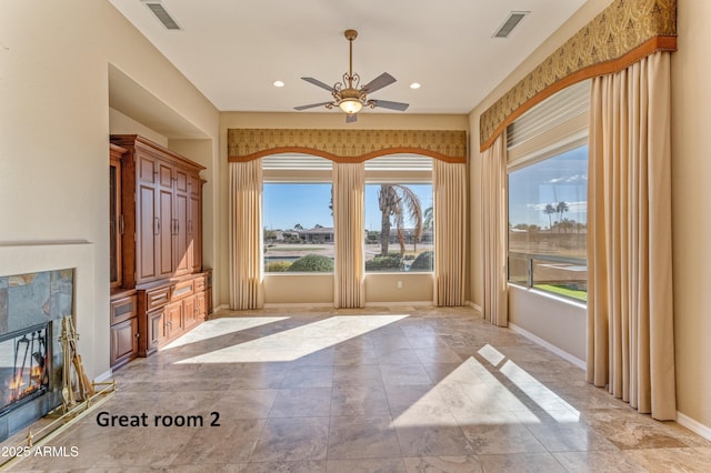 unfurnished sunroom with ceiling fan and a tile fireplace