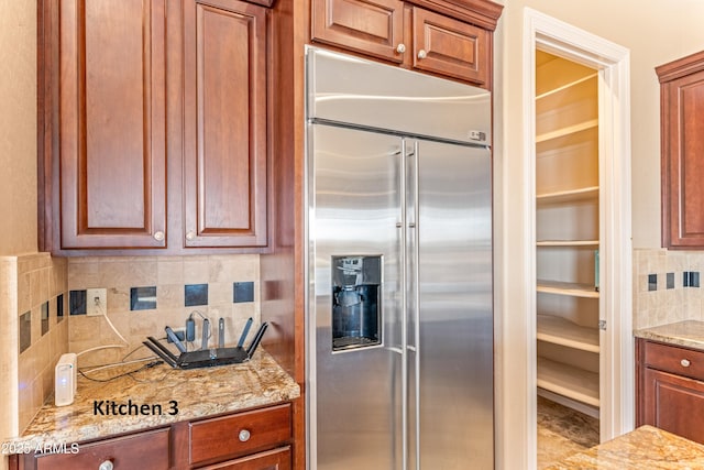 kitchen featuring built in fridge, backsplash, and light stone counters