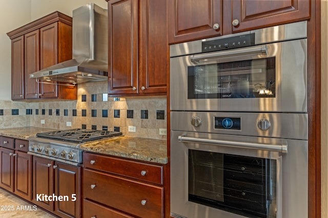 kitchen featuring light stone countertops, appliances with stainless steel finishes, wall chimney exhaust hood, and tasteful backsplash