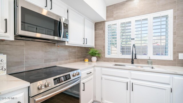 kitchen with sink, stainless steel appliances, white cabinetry, and light stone countertops