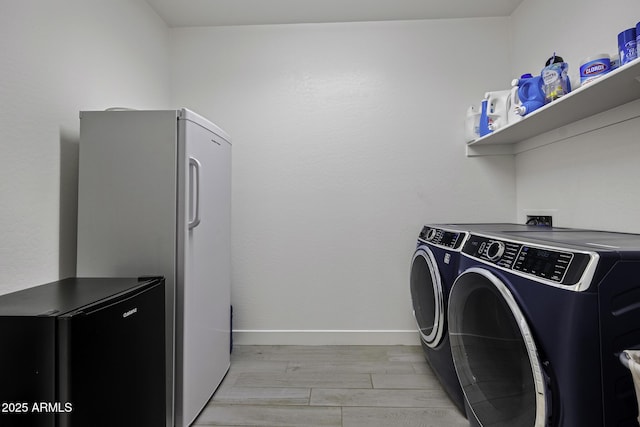 clothes washing area featuring light wood-type flooring, laundry area, washing machine and dryer, and baseboards