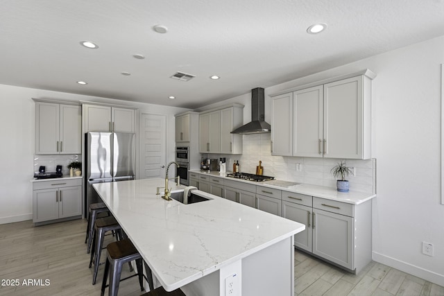 kitchen with stainless steel appliances, wall chimney range hood, visible vents, and gray cabinetry