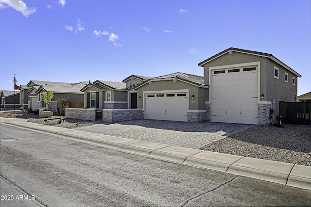 view of front of house with stone siding, an attached garage, fence, decorative driveway, and stucco siding