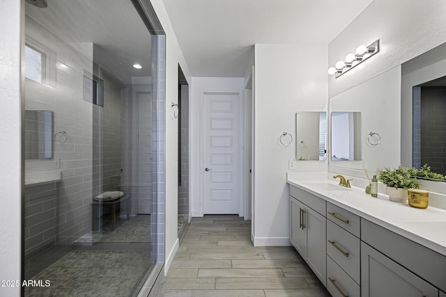 full bathroom featuring wood tiled floor, a tile shower, vanity, and baseboards