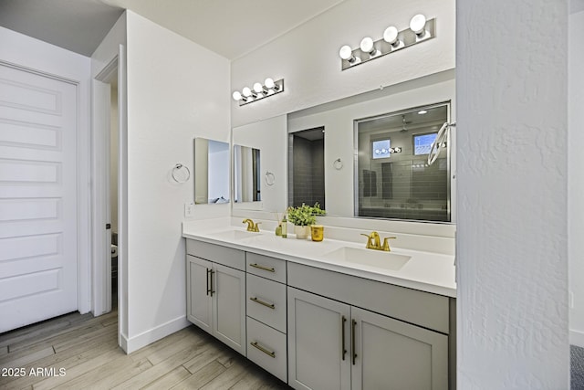 bathroom featuring double vanity, a sink, a shower stall, and wood finished floors