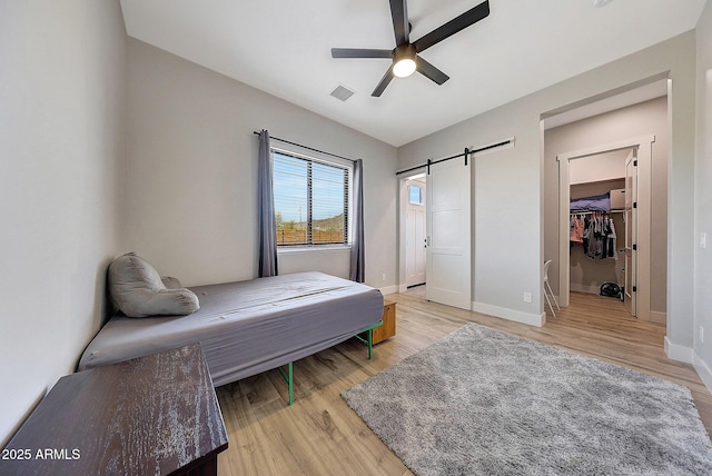 26112 N 7th Ave, Phoenix, AZ 85085 - bedroom with light wood-type flooring, a barn door, baseboards, a spacious closet, and a ceiling fan