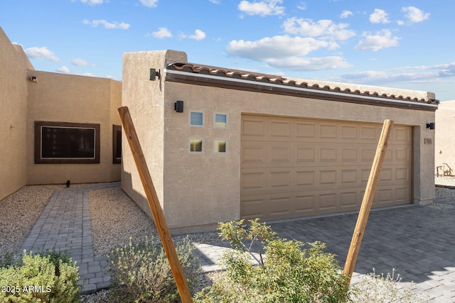 view of side of property featuring decorative driveway, an attached garage, and stucco siding