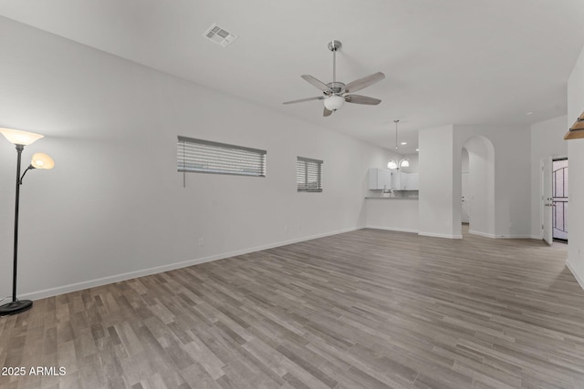 unfurnished living room featuring visible vents, arched walkways, light wood-style floors, baseboards, and ceiling fan