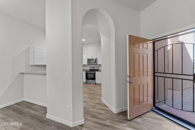 foyer entrance featuring light wood-type flooring, arched walkways, and baseboards