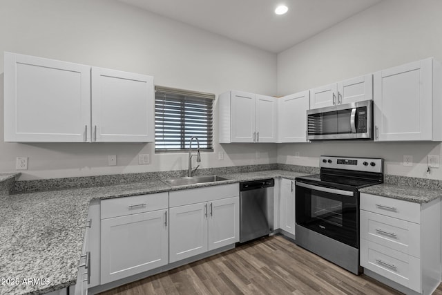 kitchen featuring light stone countertops, appliances with stainless steel finishes, wood finished floors, white cabinetry, and a sink