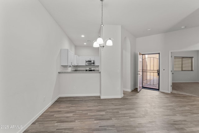 kitchen featuring baseboards, appliances with stainless steel finishes, wood finished floors, arched walkways, and white cabinets