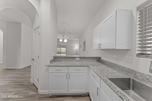 kitchen featuring light stone counters, wood finished floors, arched walkways, white cabinets, and a sink