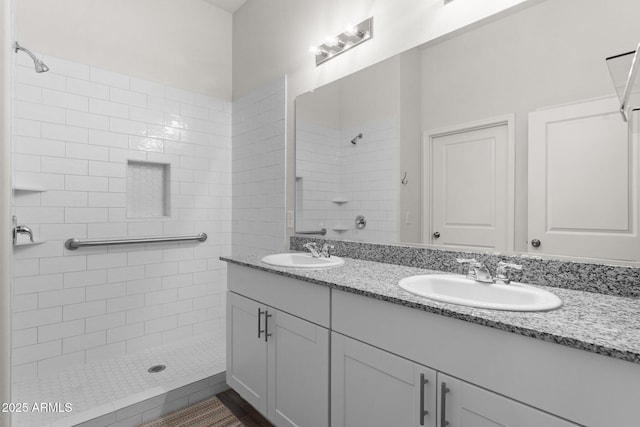 full bath featuring double vanity, tiled shower, and a sink