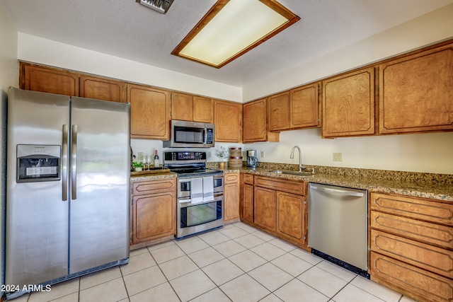 kitchen featuring stone countertops, stainless steel appliances, light tile patterned floors, and sink