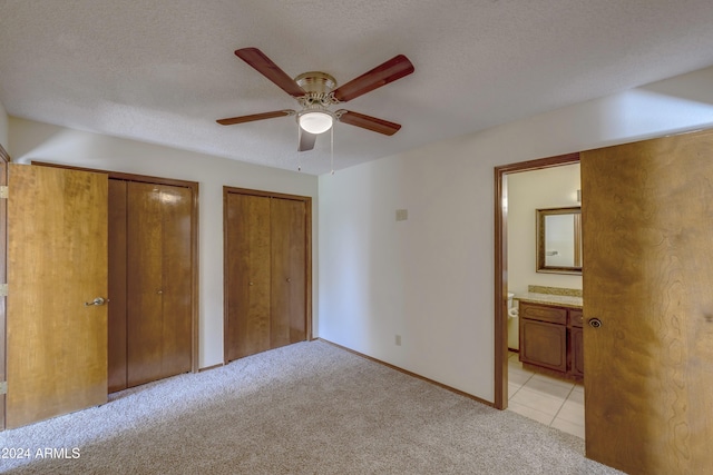 unfurnished bedroom featuring multiple closets, ensuite bathroom, ceiling fan, and light colored carpet