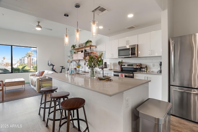 kitchen featuring sink, appliances with stainless steel finishes, white cabinetry, hanging light fixtures, and a center island with sink