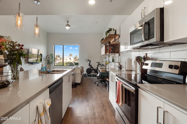 kitchen with appliances with stainless steel finishes, dark hardwood / wood-style floors, sink, white cabinets, and hanging light fixtures